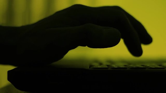 Shadow, silhouette of a male palm hand, typing on the laptop keyboard in the darkness.