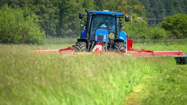 A farmer is driving on his blue tractor and he needs to cut a large field with its grass cutting machinery.
