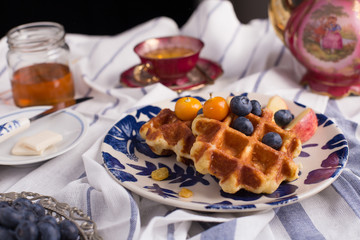 Blueberry apple waffle with honey set on a dish decorated with fresh blueberry, apple and almond.