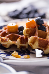 Blueberry apple waffle with honey set on a dish decorated with fresh blueberry, apple and almond.