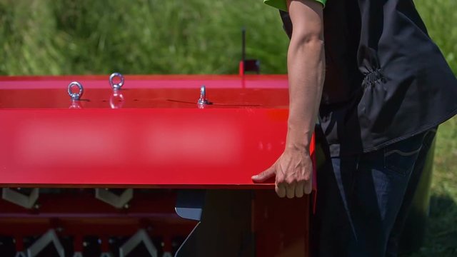 A young man is lifting up and down grass cutting machinery with his hands. Then he goes to the other side to check the same.
