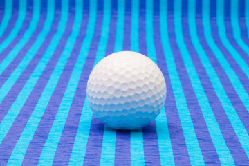 White golf ball on blue striped table.