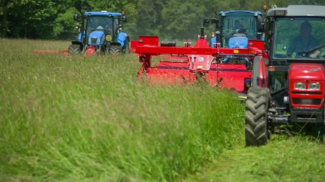Three large tractors are cutting grass on a big meadow. They are connected to three cutting grass machineries. The meadow is huge.
