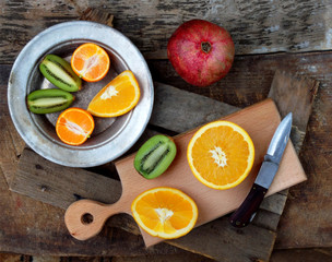 composition of the cut fruit, orange, kiwi, tangerine, pomegranate on a wooden board and a plate. Selective focus