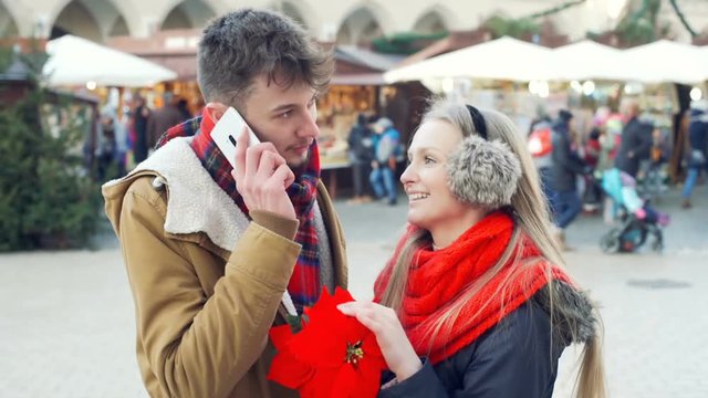 Girl holding poinsettia while her boyfriend chatting on cellphone, steadycam shot
