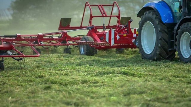 Two big tractors are driving across the field and are organizing freshly cut grass. There are rotary rakes connected to them.
