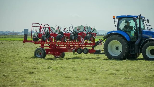 A young farmer is coming on the field with his tractor and rotary hay rakes and he will begin working and preparing hay.
