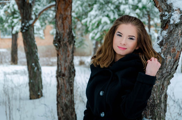 smiling young girl walking winter forest, Beautiful girl on a walk winter park. Girl with magnificent long hair among trees in the snow. Fashionable girl in winter coat in the snowy park.

