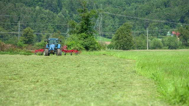 A man is working on his tractor. He lowers down rotary hay rakes and start preparing hay. It is a hot summer day.
