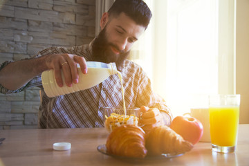 bearded man having breakfast with cornflakes, milk and croissant