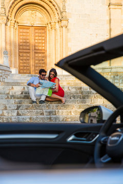Young couple with convertible sitting on church stairway looking at map, Calvia, Majorca, Spain