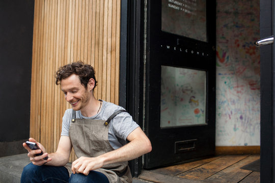 Waiter taking a break on cafe step looking at smartphone