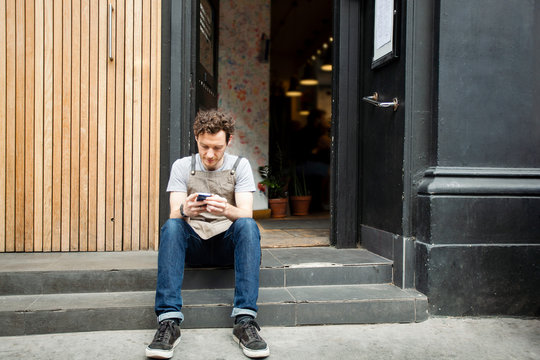 Waiter taking a break on cafe step looking at smartphone