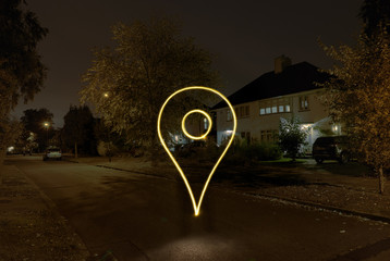 Light painted drop pin symbol floating on suburban street at night
