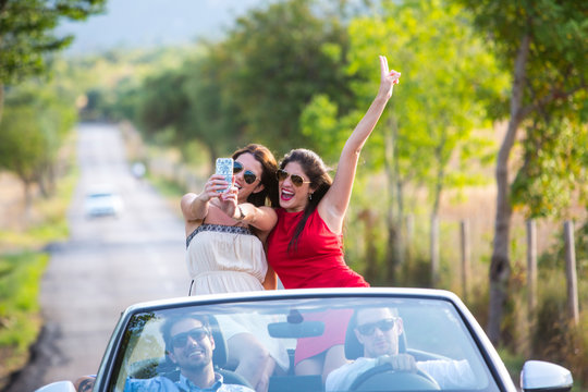 Two young female friends taking selfie whilst driving on rural road in convertible, Majorca, Spain