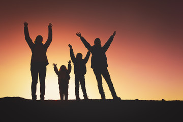 Silhouettes of happy family with two kids hiking at sunset