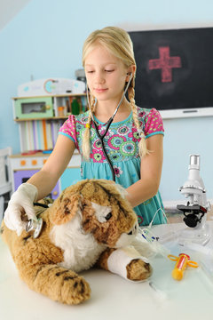 Girl pretending to be vet examining toy tiger using stethoscope