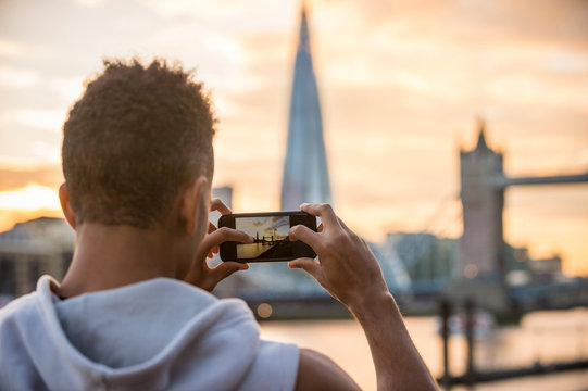 Man by riverside taking photograph of Tower Bridge and The Shard, Wapping, London, UK