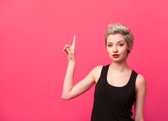Woman showing up with her finger on pink background.