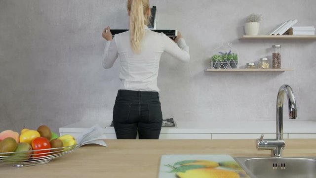 A young woman is standing on a stool in her kitchen and she is adjusting the kitchen hood in her kitchen and she is using spirit level.
