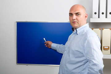 Lehrer erklärt einen Sachverhalt an einer blauen Tafel
