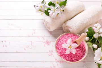 Pink sea salt in bowl, towels  and flowers on white wooden backg