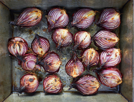 Roasted red onion halves with rosemary and olive oil in roasting tin
