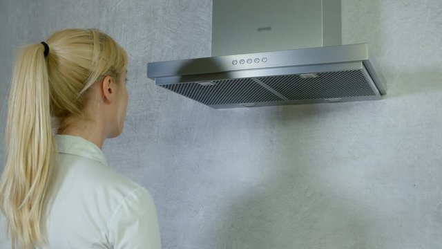 A young woman is carefully putting down a filter from the kitchen vent and then she is putting it back up.
