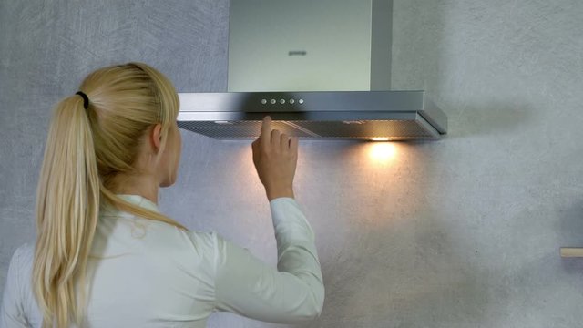A young woman comes to the kitchen vent. She turns on a button and the lights turn on. Then she is pressing a few different buttons and then at the end, the lights turn off.
