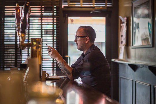Barman sitting at bar counter with smartphone