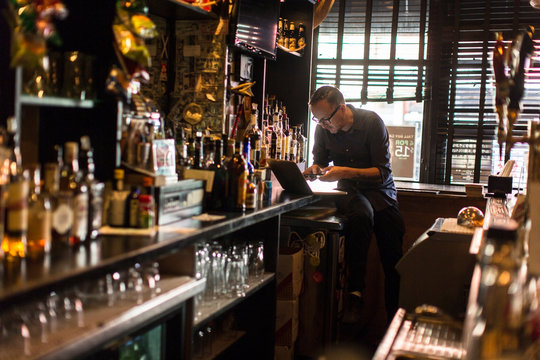 Barman typing on laptop at public house counter