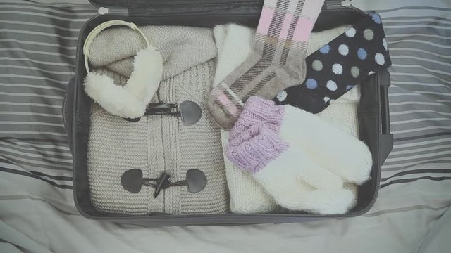 top view of a girl who prepares the suitcase to go to the mountains with hat, earmuffs, gloves, sweater and sunglasses