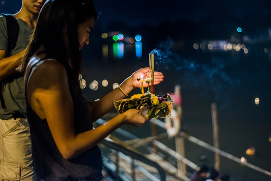 Young woman by Ping River in Chiang Mai during Loy Krathong Lantern Festival, releasing floating lantern down the Ping River, Chiang Mai, Thailand