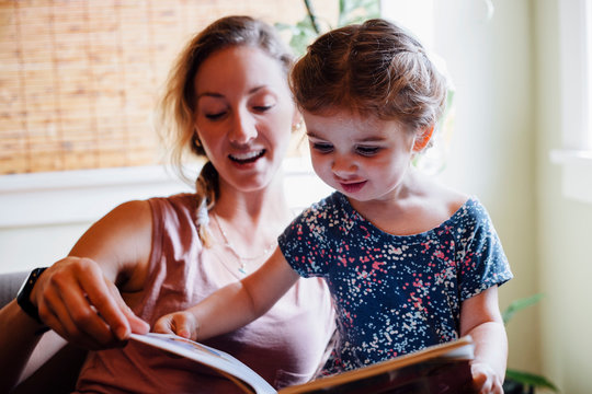 Woman on sofa with toddler daughter reading storybook