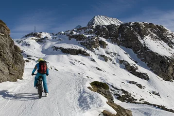 Fotobehang Sciatore con ebike - mountain bike elettrica - fat bike da neve, che sale in alta montagna con gli sci caricati sulla bici, Riale, Val Formazza, Ossola, Alpi Italia © Angela
