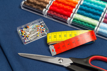textile sewing equipment scissors measuring tape and pins on blue cotton fabric