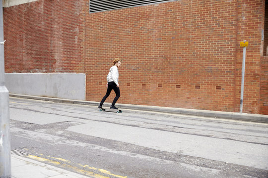 Red haired man skateboarding on an urban road, side view