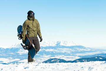 Fototapeta na wymiar Male snowboarder holding his board in hand and taking a walk at the top of a mountain