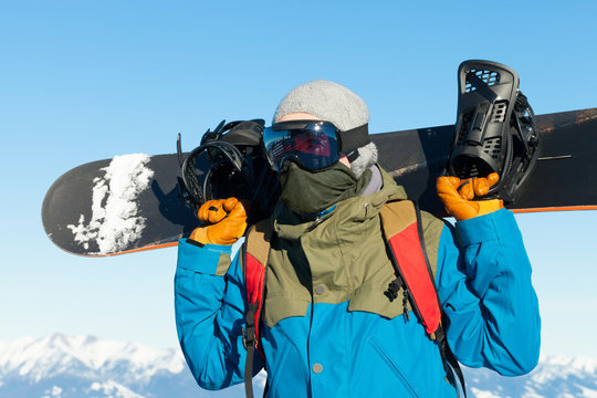 Male snowboarder holding board behind his sholders at the very top of a mountain