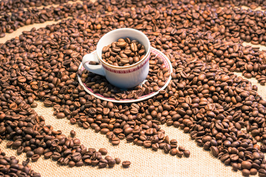 Coffee cup full of beans emerging from wavy grain heap close up image with blurred background 