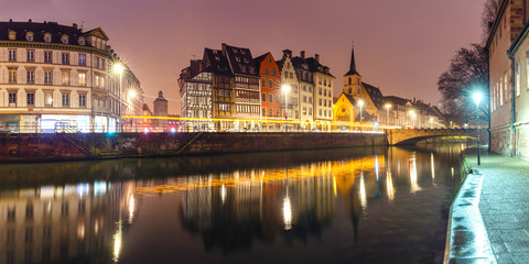 Fototapeta na wymiar Picturesque panorama of quay and church of Saint Nicolas with mirror reflections in the river Ile during morning blue hour, Strasbourg, Alsace, France