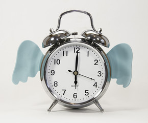 Time flies represented by a vintage silver alarm clock with blue wings against a white background