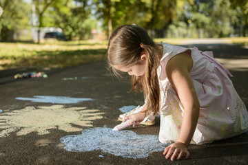 Little girl drawing on asphalt with chalk in a sunny summer day. Concept of child imagination