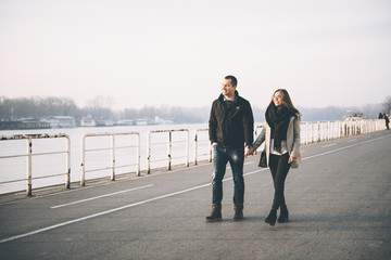 People in love theme. Attractive young couple enjoying in urban city outdoors. They walking by the river, holding hands and talking.