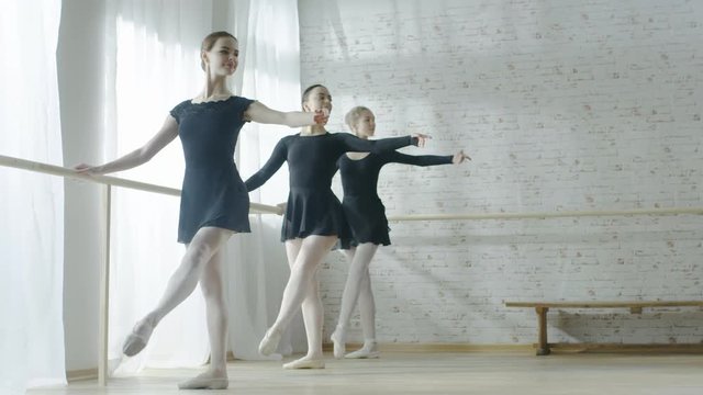  Long Shot of Three Amazing Young Ballerinas Doing Morning Stretching Routine Near Bar. Shot on a Bright and Sunny Morning in Modern Studio. Shot on RED EPIC-W 8K Helium Cinema Camera.