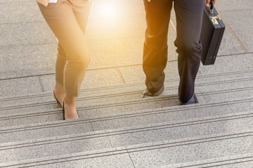 Businessman and Business woman walking up stairs with bags to office.