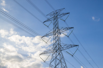 Electricity pylon silhouetted against blue sky wih cloud background. High voltage tower
