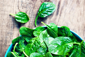Spinach leaves in a bowl on rustic wooden table close up with co