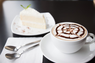 Hot cappuccino and cake on a black table.