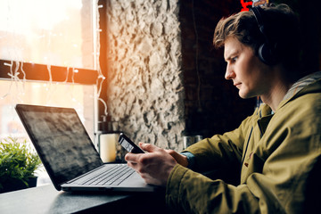 Man in a cafe working on the computer and listening to music on headphones. Concept of technology...